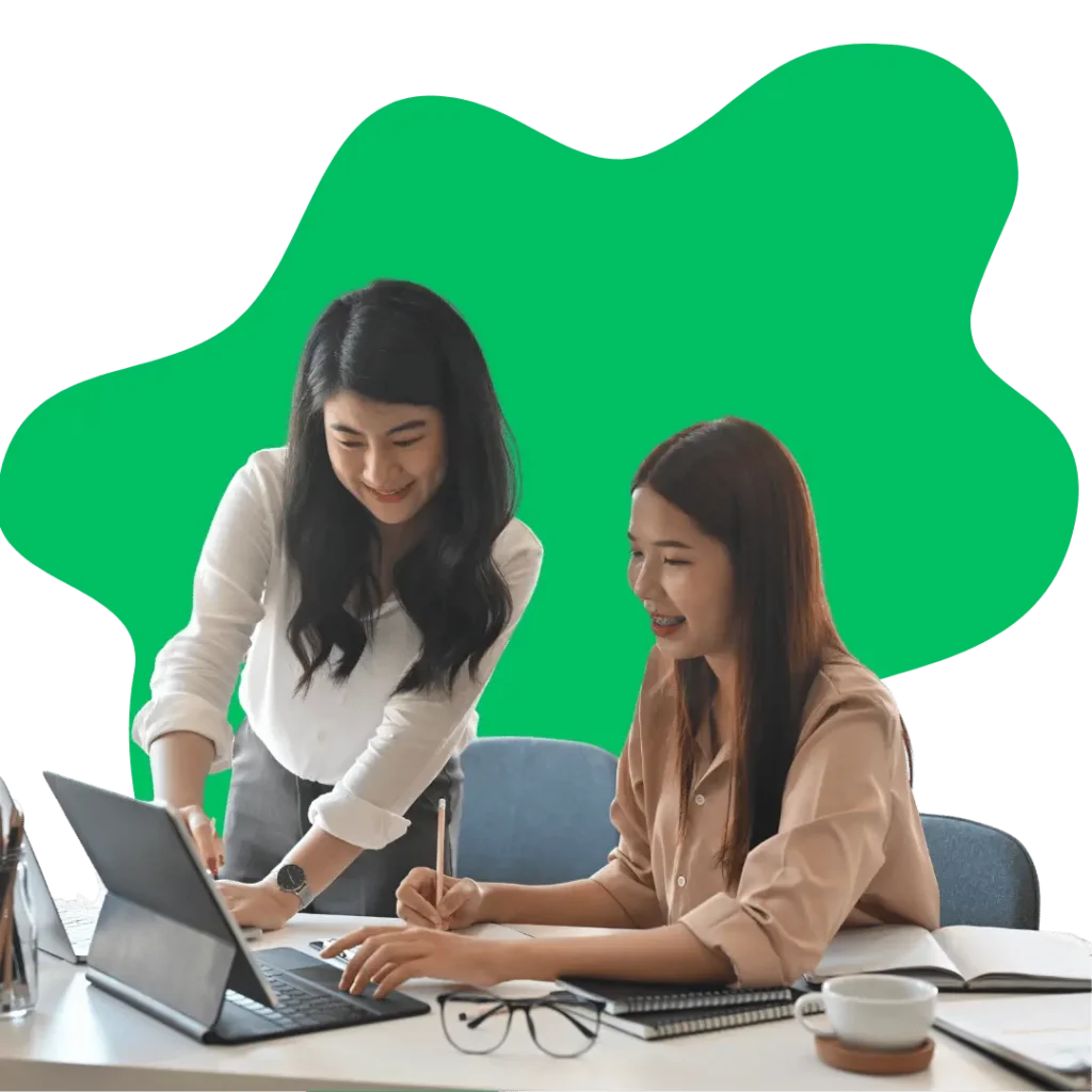 Two women working together on a laptop and taking notes, representing the collaborative benefits of our workflow automation solutions.