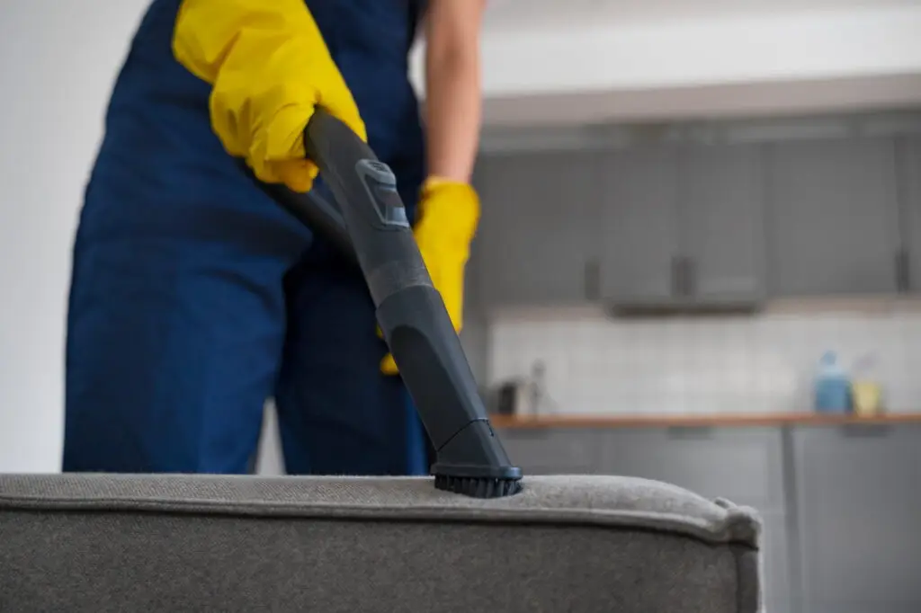 Woman using a vacuum cleaner to clean a couch in a modern kitchen, emphasizing home cleaning services relevant to carpet cleaning SEO strategies.