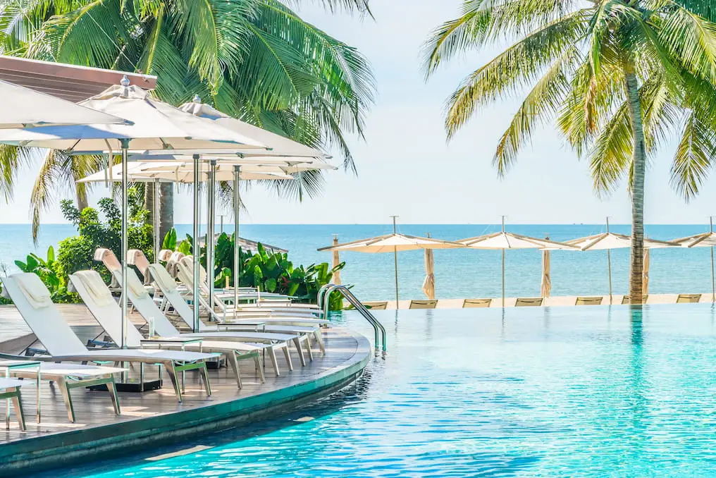 Luxury hotel poolside with lounge chairs, umbrellas, and ocean view, highlighting resort amenities for enhancing guest experience and direct bookings.